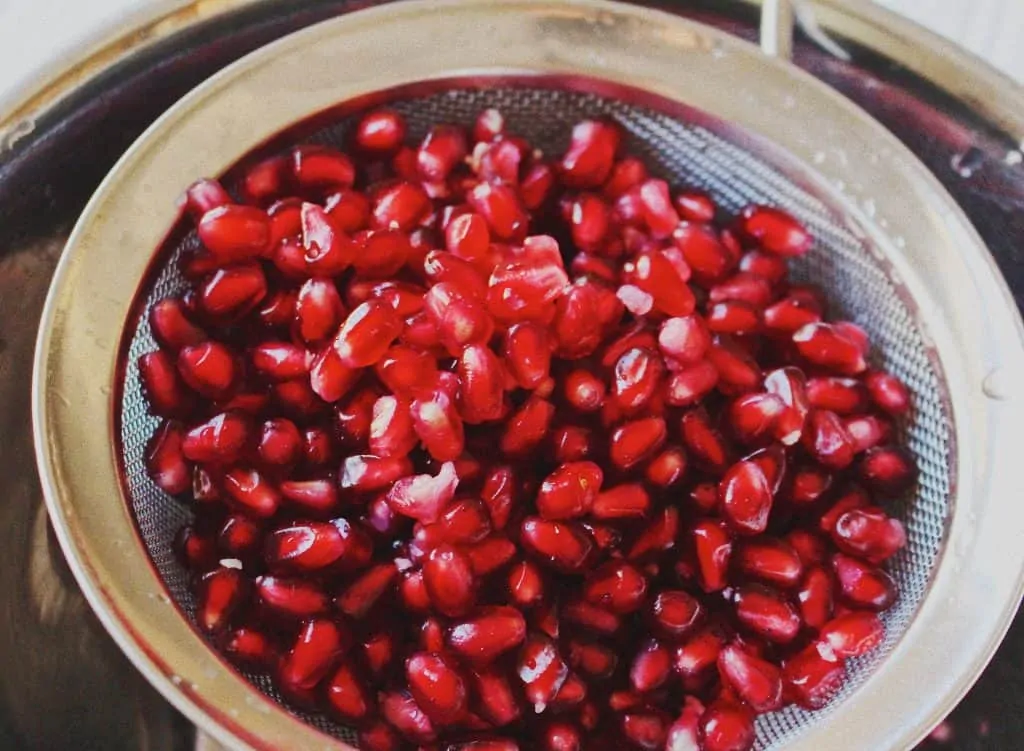 pomegranate arils in strainer for roasted winter salad