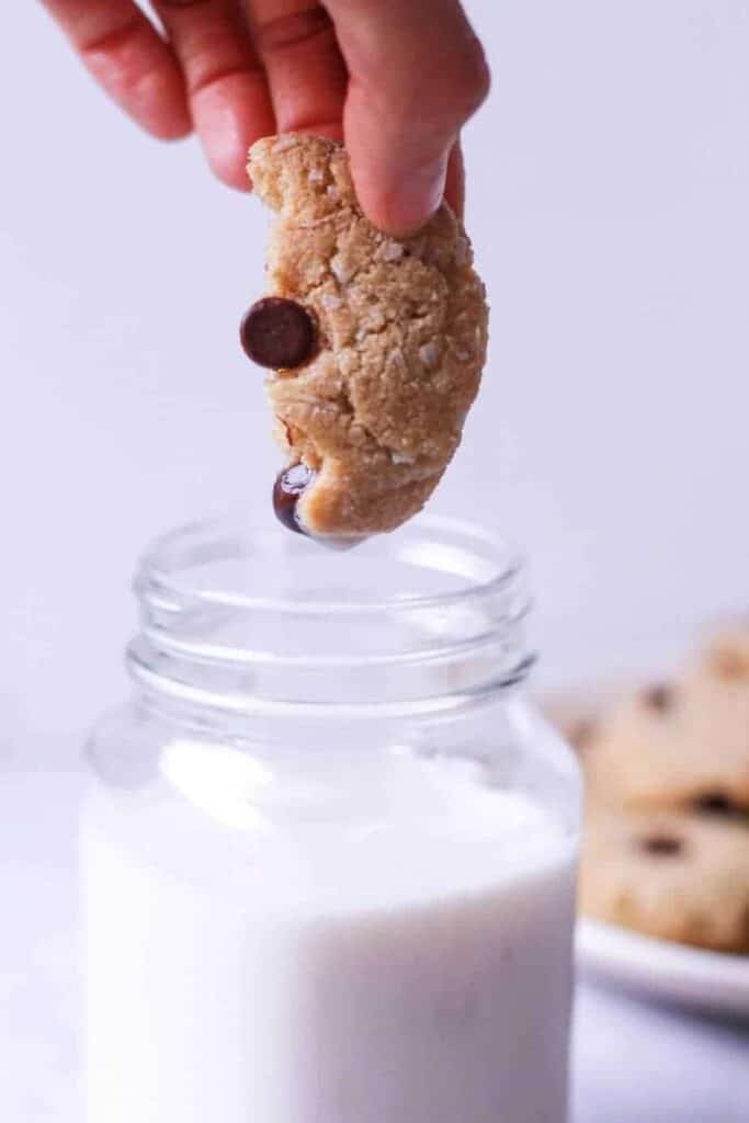 closeup of keto coconut chocolate chip tahini cookie dunked in a glass of almond milk
