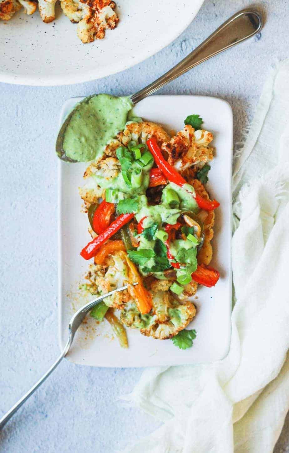 overhead of fajita cauliflower steak with cilantro avocado dressing on a plate