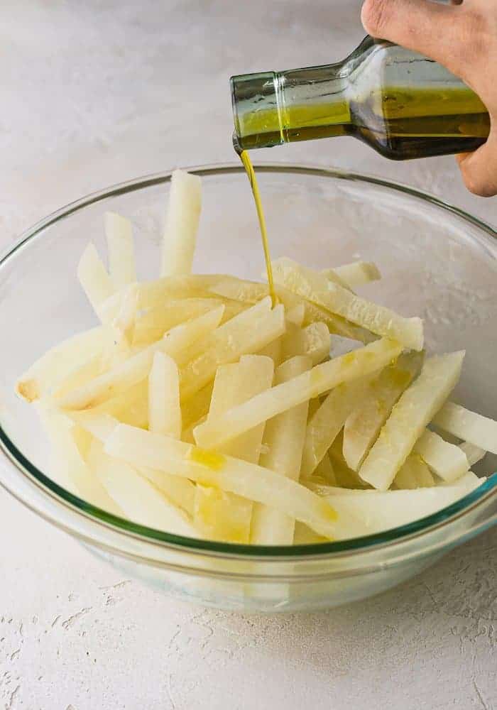 pouring olive oil on jicama fries