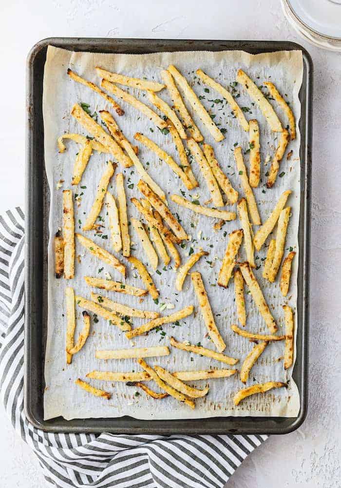 overhead of cilantro garlic jicama fries on a sheet pan with plates and a striped napkin
