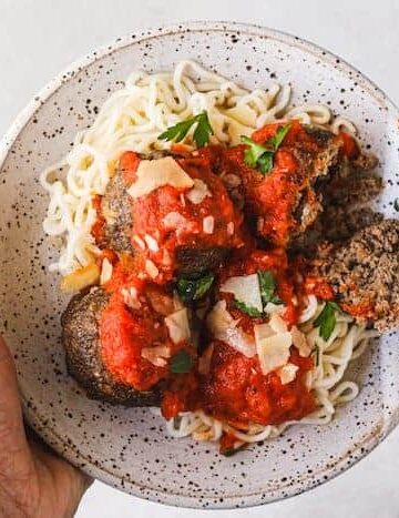 holding a plate of keto Italian meatballs and spaghetti