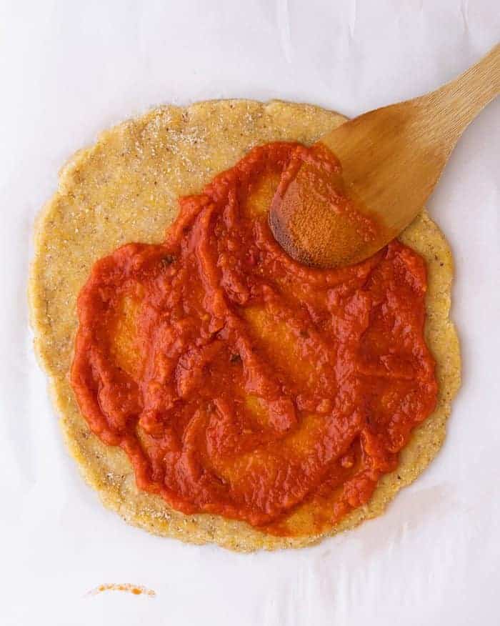 spreading sauce on almond flour pizza crust