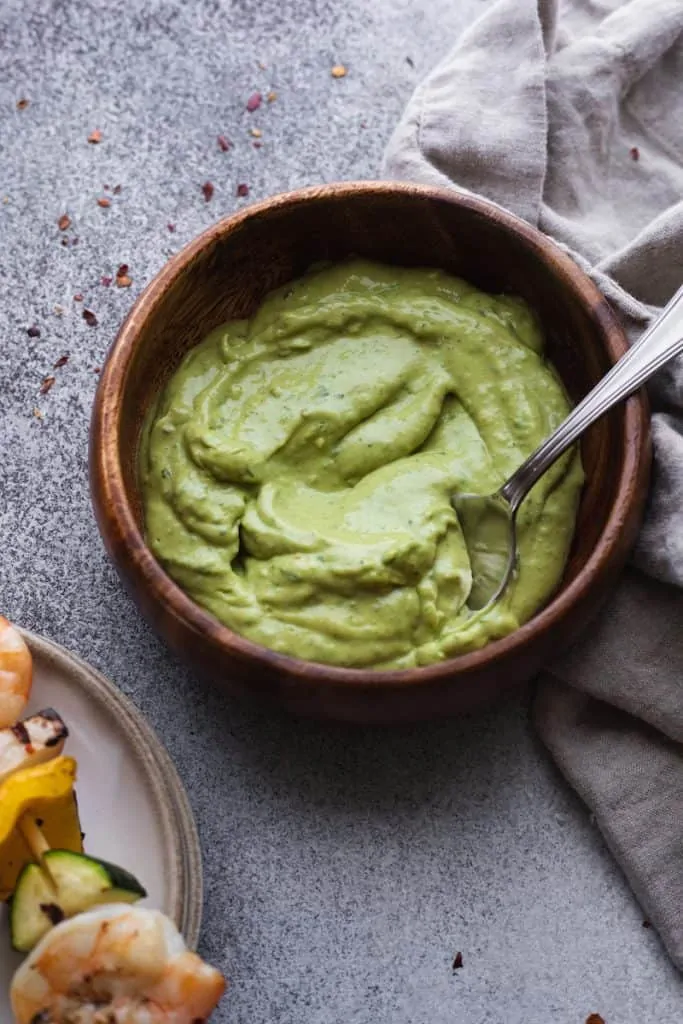 basil avocado sauce in a wooden bowl with a spoon