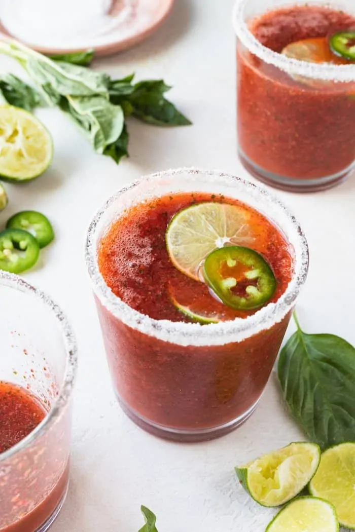 strawberry basil margaritas in three glasses with basil and lime
