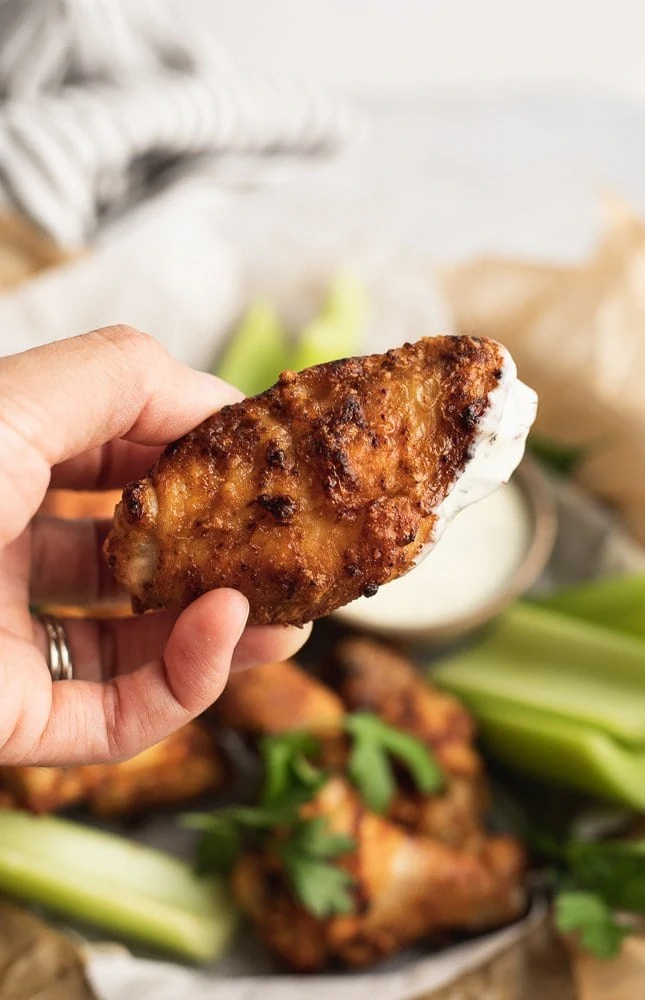 holding an air fryer chicken wing dipped in ranch