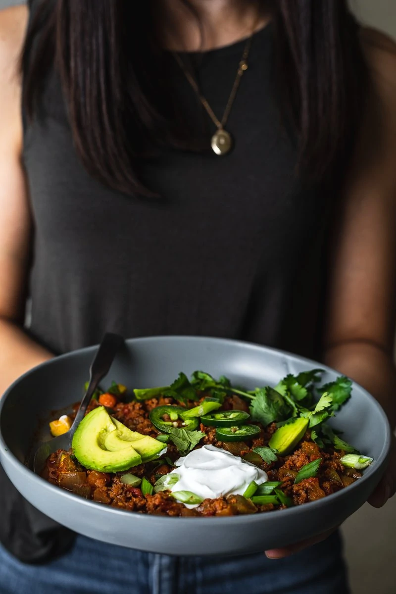 holding a bowl of keto chili with toppings