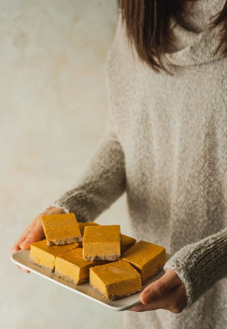 woman holding a plate of keto pumpkin cheesecake bars