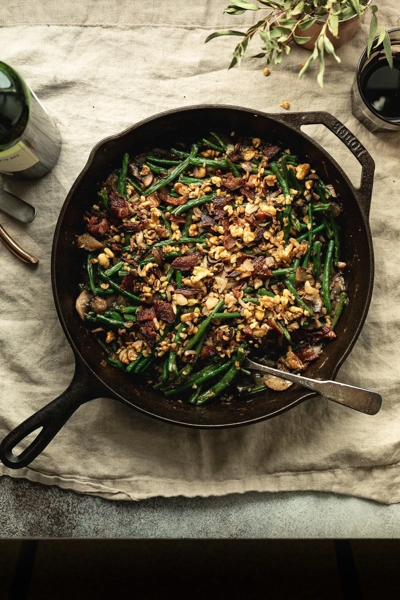 Keto green bean casserole in a cast iron skillet with walnut and bacon topping