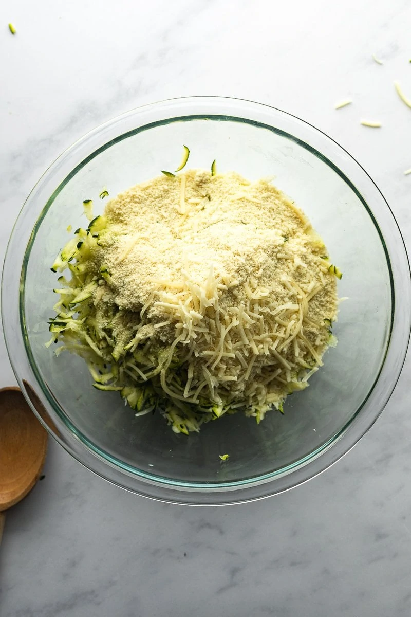 Ingredients for keto zucchini fritters in a glass mixing bowl.