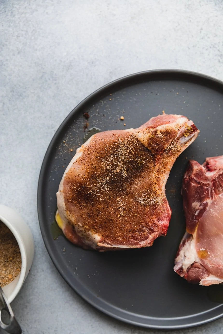 Bone-in air fryer pork chops on a gray plate with seasoning mixture.