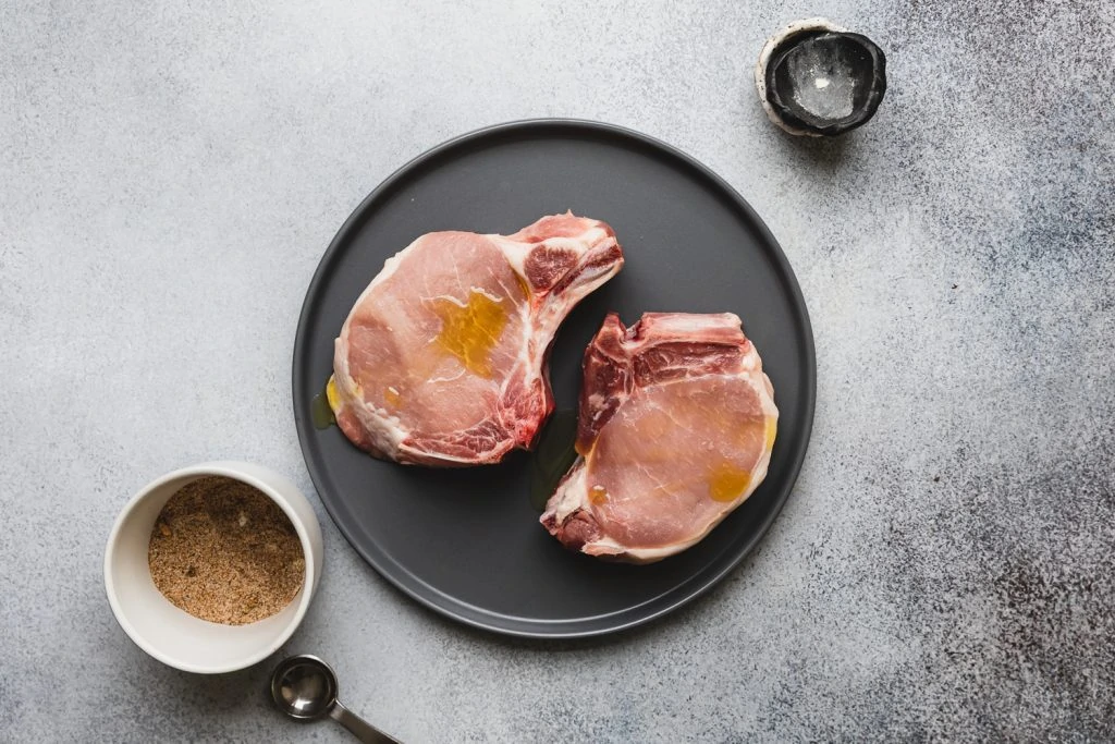 raw pork chops on gray plate with olive oil
