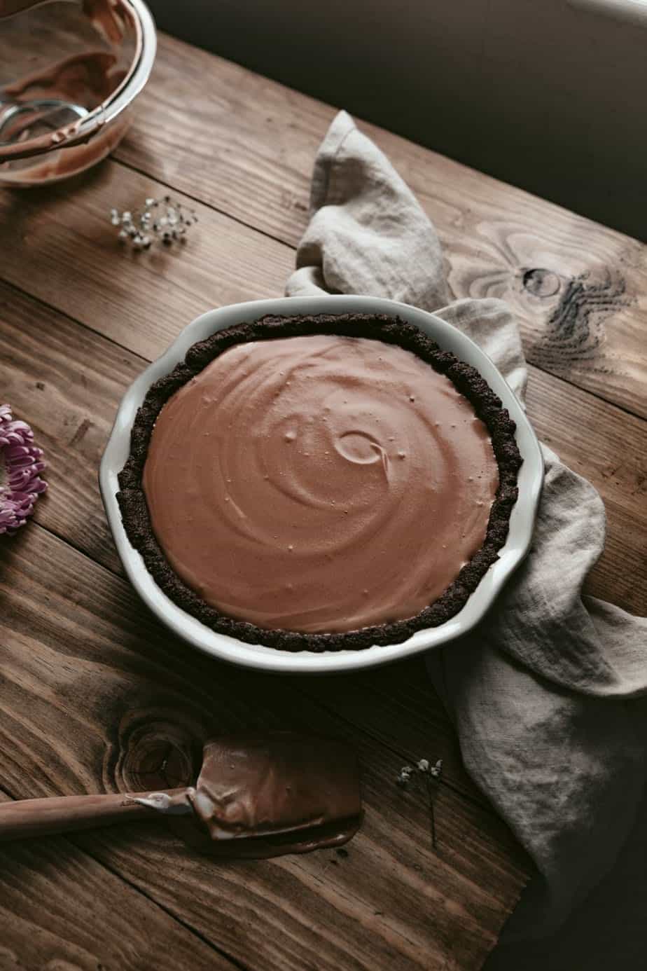 A cocoa crust filled with the chocolate mousse in a pie dish on a wooden table.