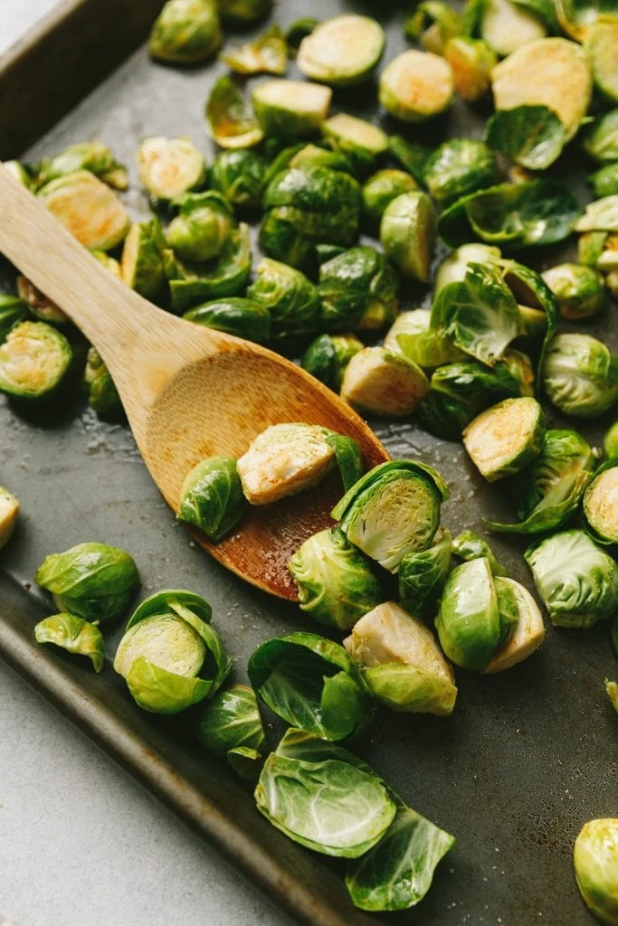 raw Brussels sprouts on a sheet pan with wooden spoon
