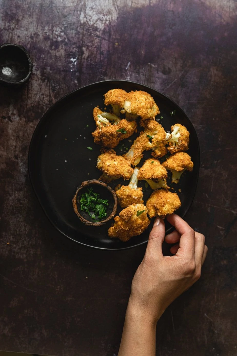 Air fried cauliflower on a black plate with chopped parsley on the side. 