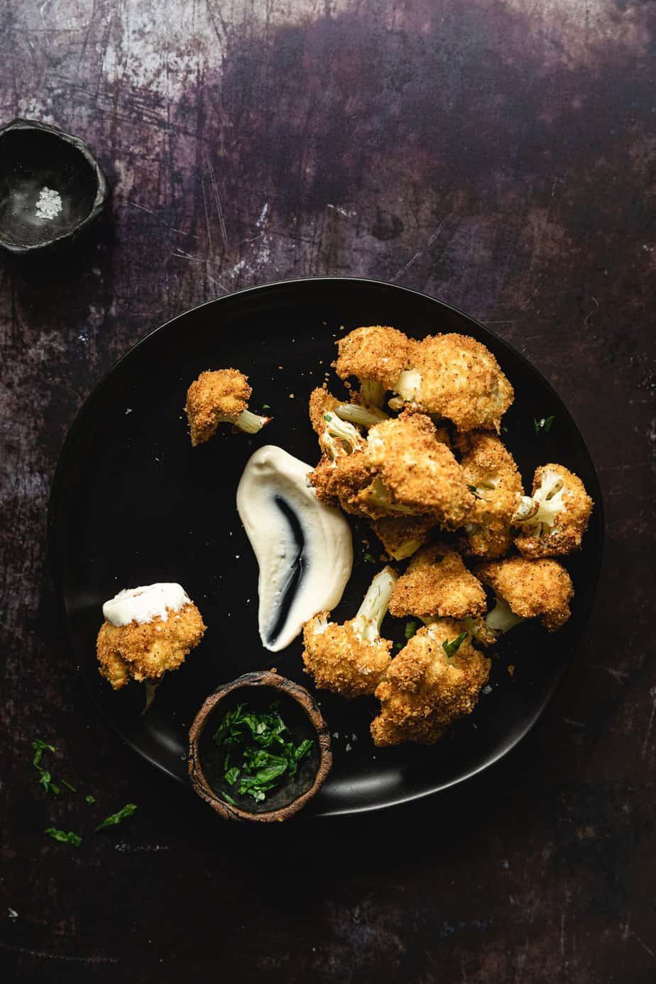 Air fried cauliflower pieces with a dipping sauce on a black plate.