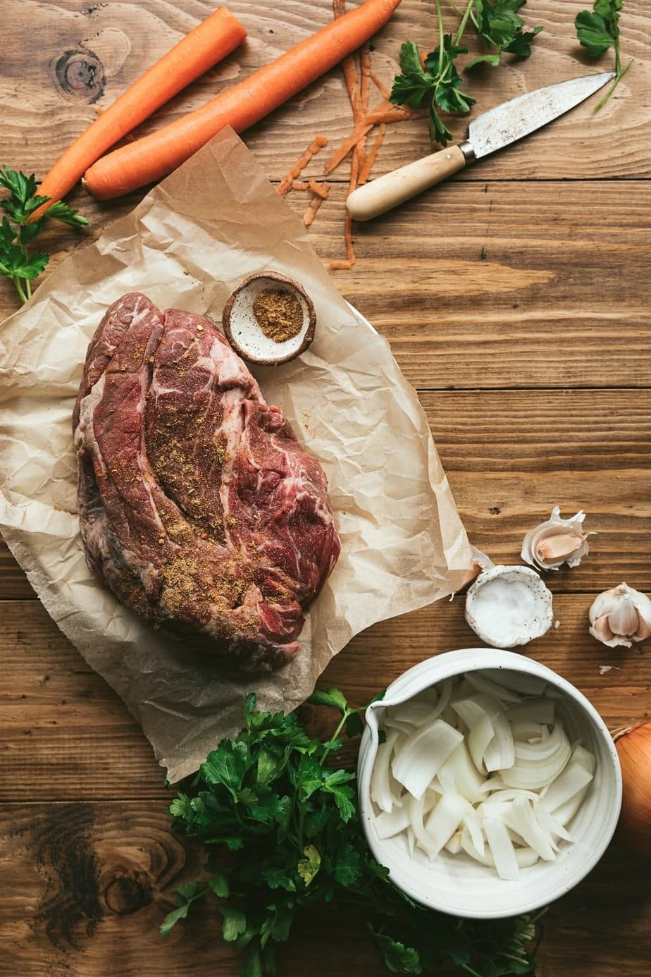 raw chuck roast with chopped onions and carrots on a wooden table