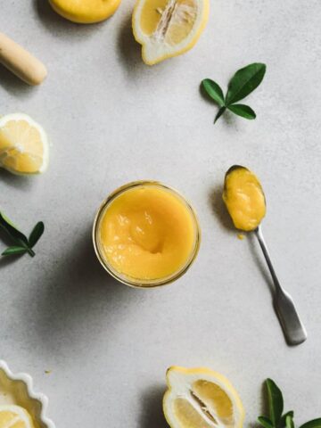 jar of keto lemon curd with a spoonful next to it and lemons arranged in flat lay