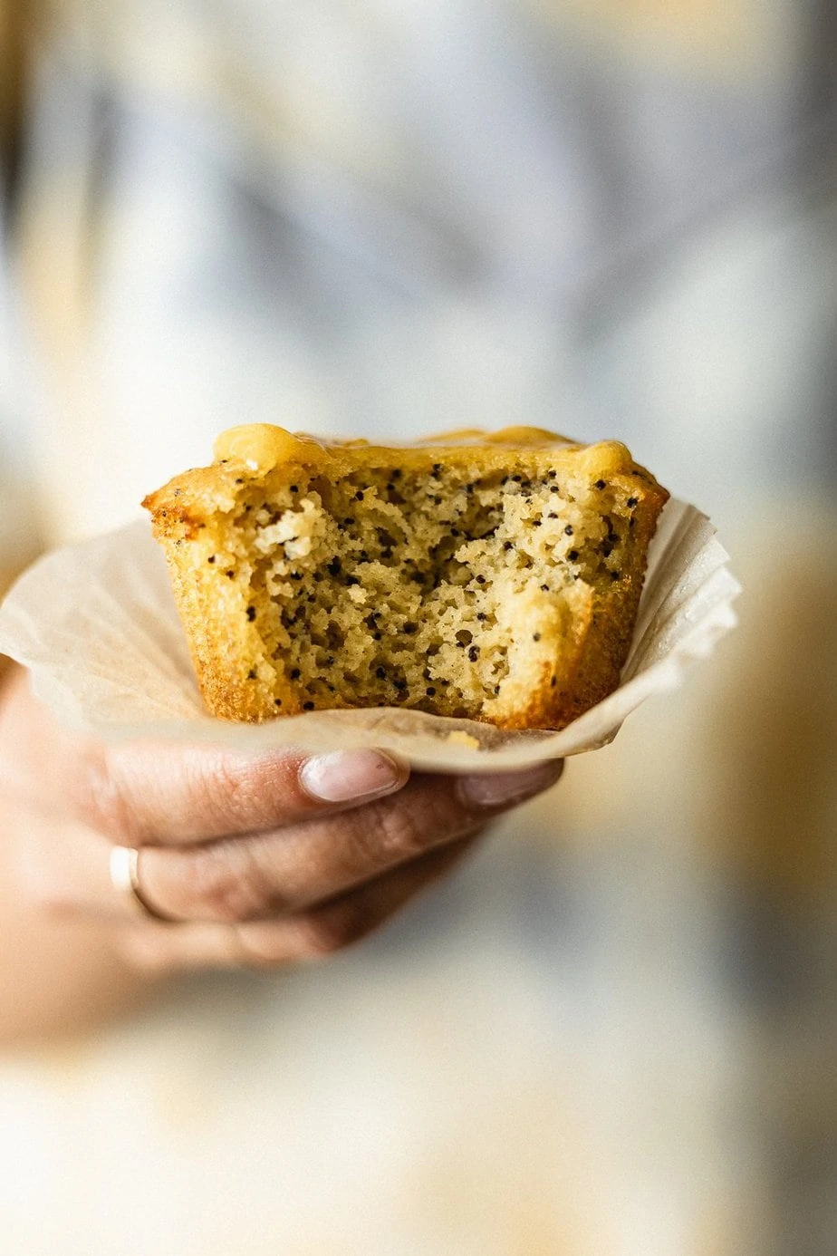 A hand holding a healthy lemon poppy seed muffin with a bite taken out.