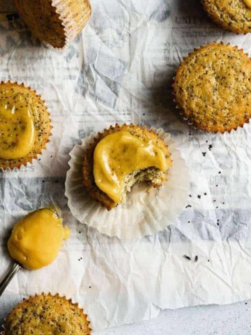 keto lemon poppy seed muffins arranged on top of parchment paper with lemon curd