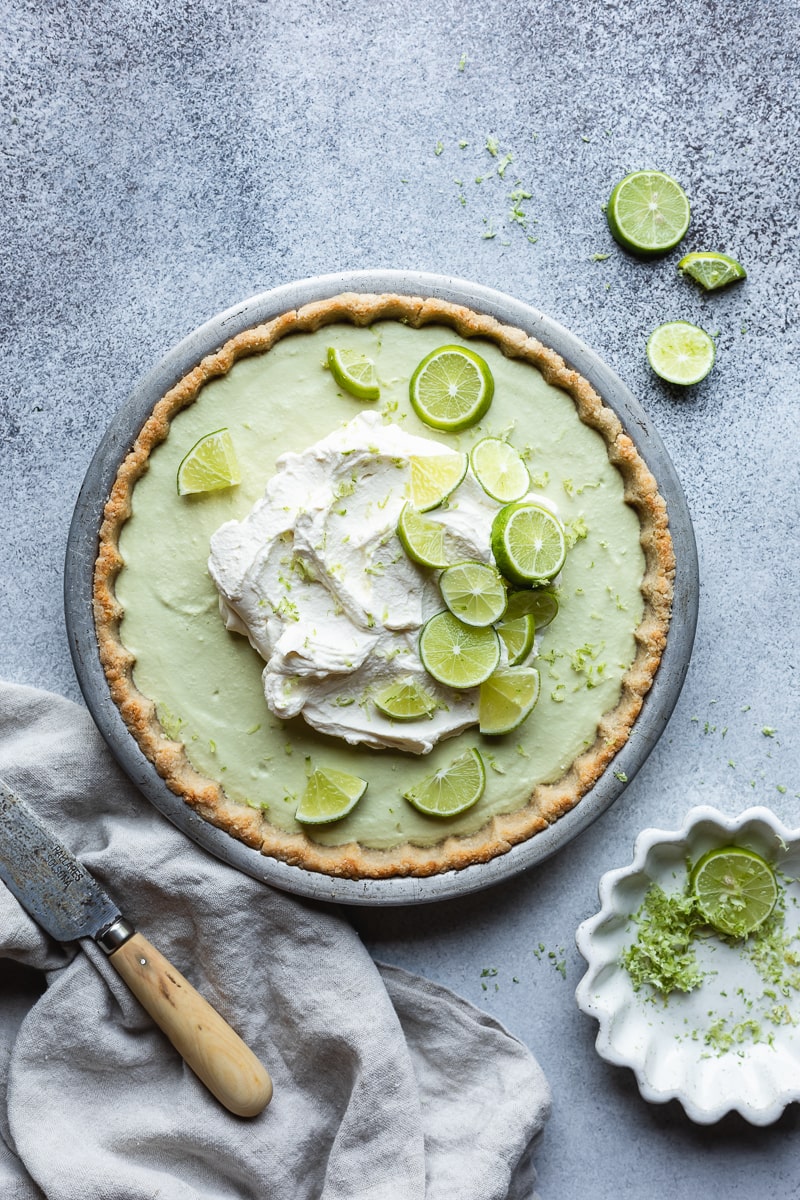 Keto key lime pie in a pie plate with lime wedges and whipped cream on top.