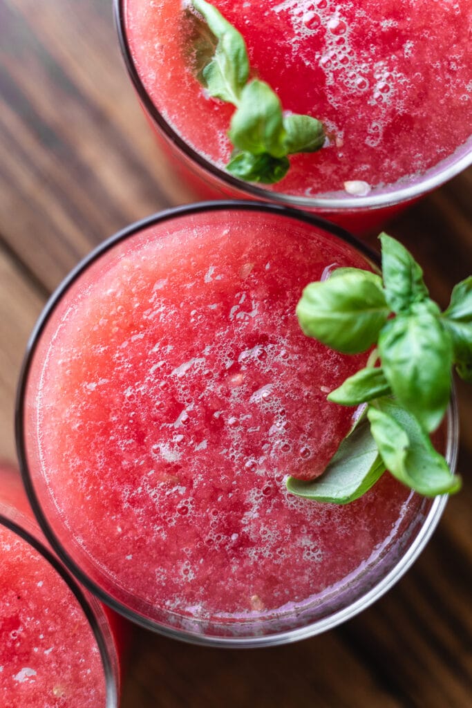 closeup of the top of a glass of watermelon slushie garnished with basil