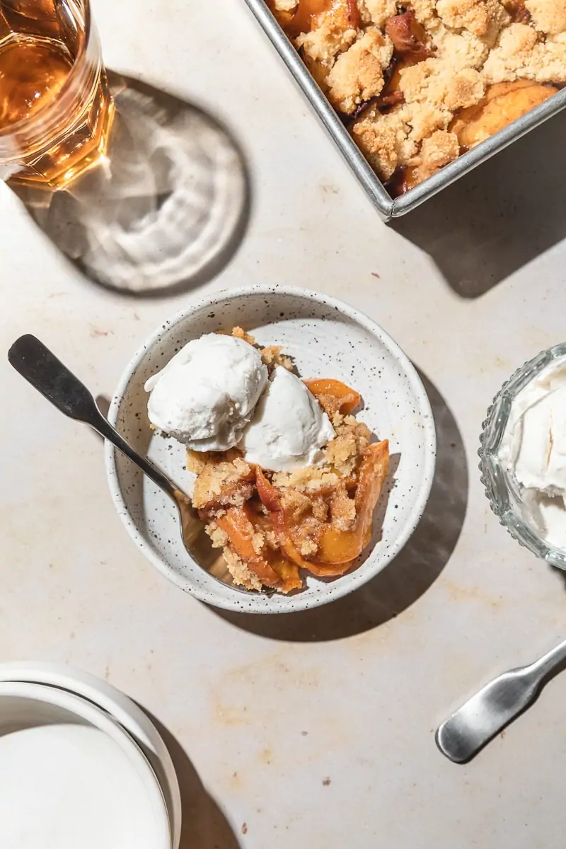 Warm keto peach cobbler in dish with ice scream scoops on top.