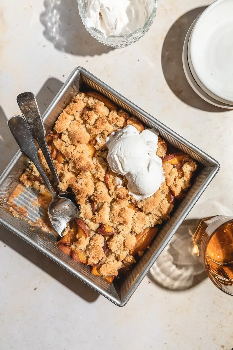 Keto peach cobbler in baking dish with scoop of ice cream. 