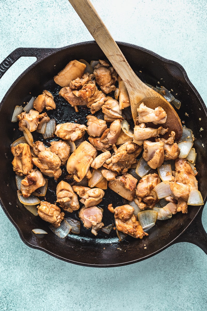 chicken and onions in a cast iron skillet with a wooden spoon