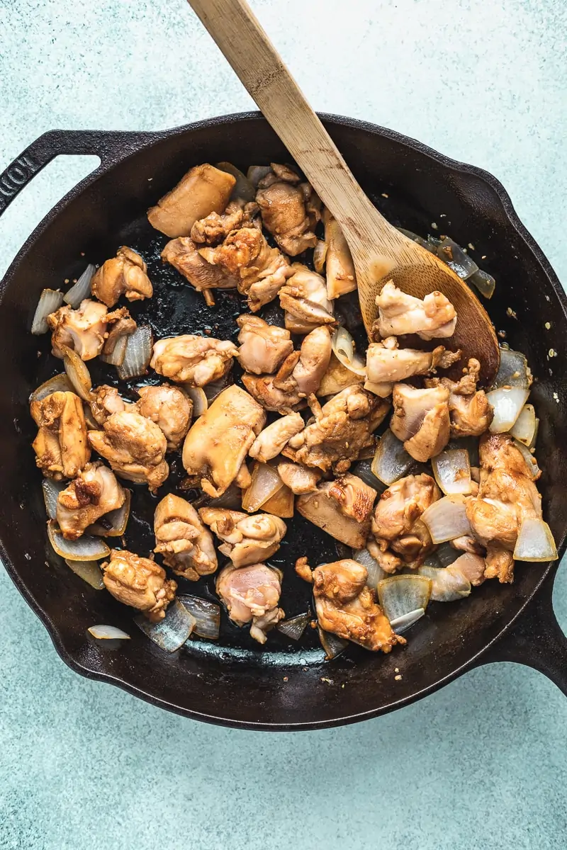 chicken and onions in a cast iron skillet with a wooden spoon
