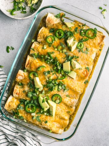 green chicken enchiladas in a casserole dish with toppings