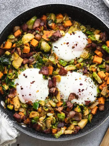 Brussels sprouts hash in a pan with a wooden spatula and cooked eggs on top