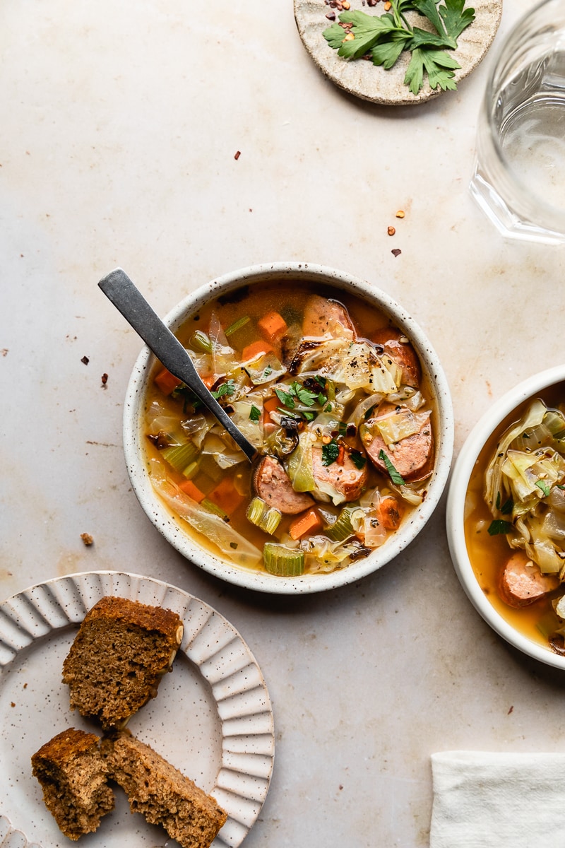 two bowls of keto cabbage sausage soup with a glass and low-carb bread