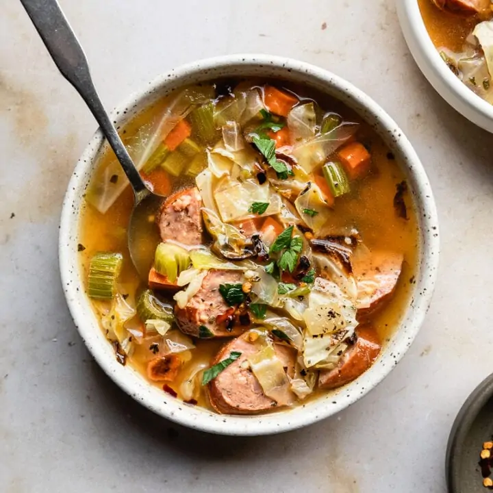 bowl of cabbage sausage soup on marble backdrop with a spoon