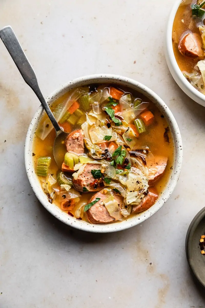 bowl of cabbage sausage soup on marble backdrop with a spoon