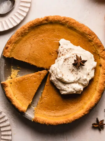keto pumpkin pie with a slice cut out and whipped cream on top