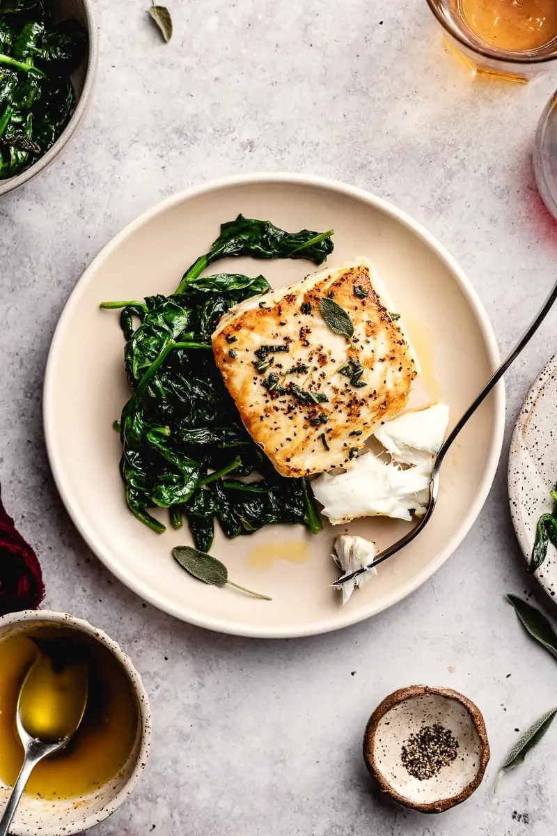 Pan-seared halibut on a plate with spinach and water glasses around it.