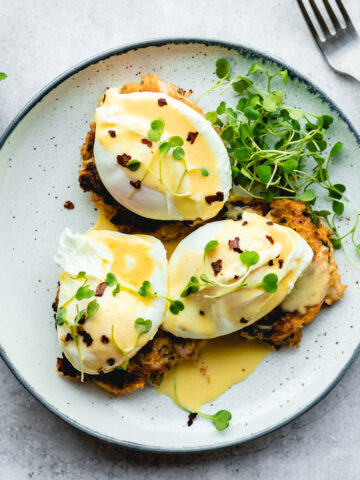 crab cake Benedict on a plate with microgreens and a red pepper flakes
