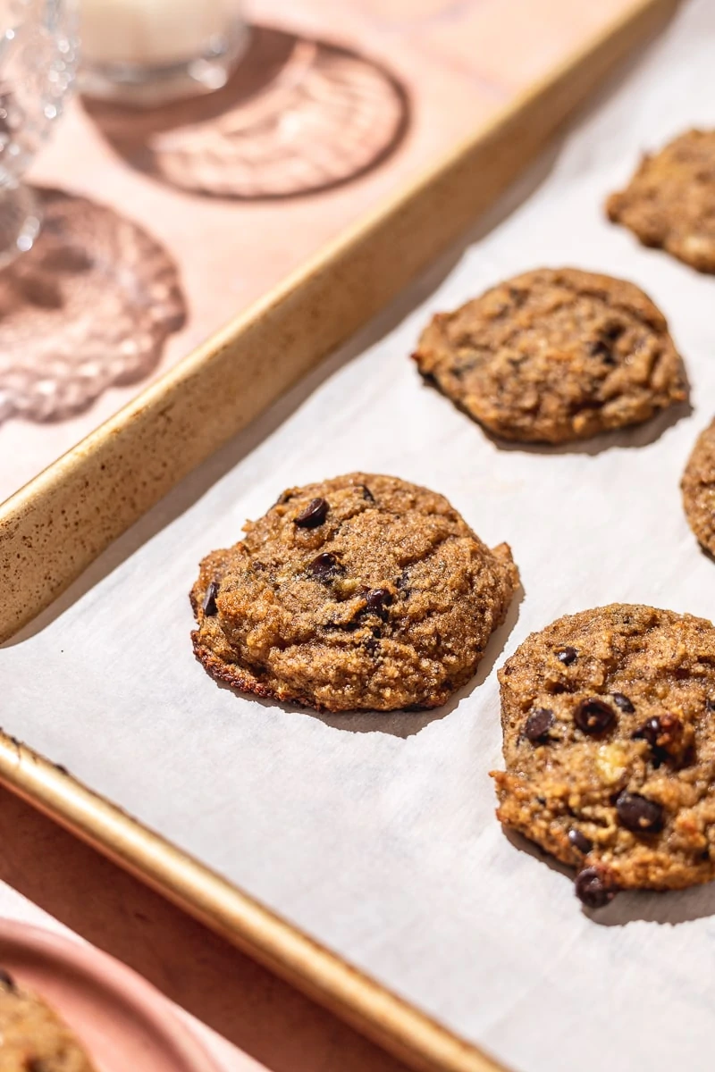 close up of almond flour banana cookies on a gold baking tray with pink background