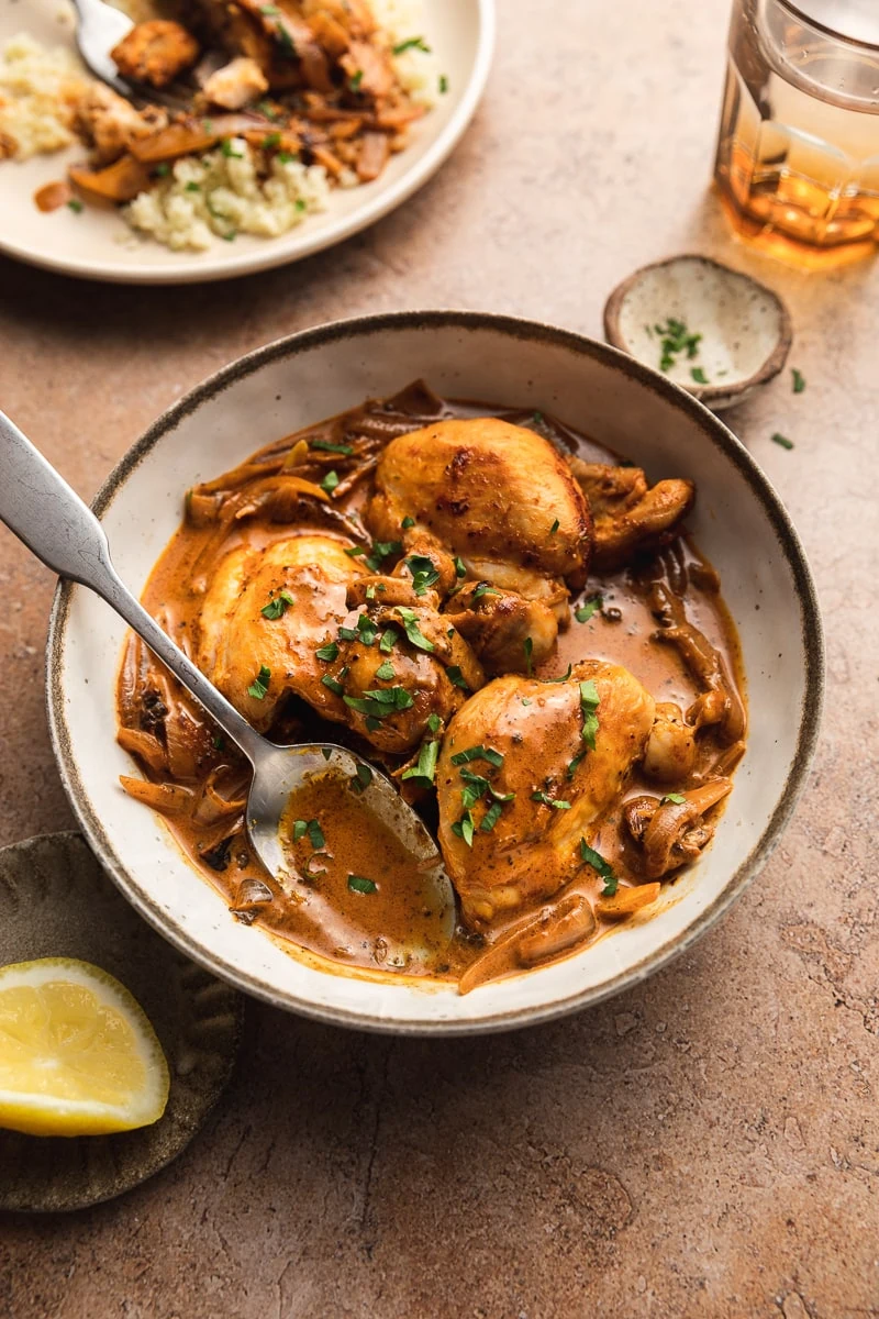 Creamy paprika chicken thighs with sauce in a serving bowl with a spoon and parsley garnish.
