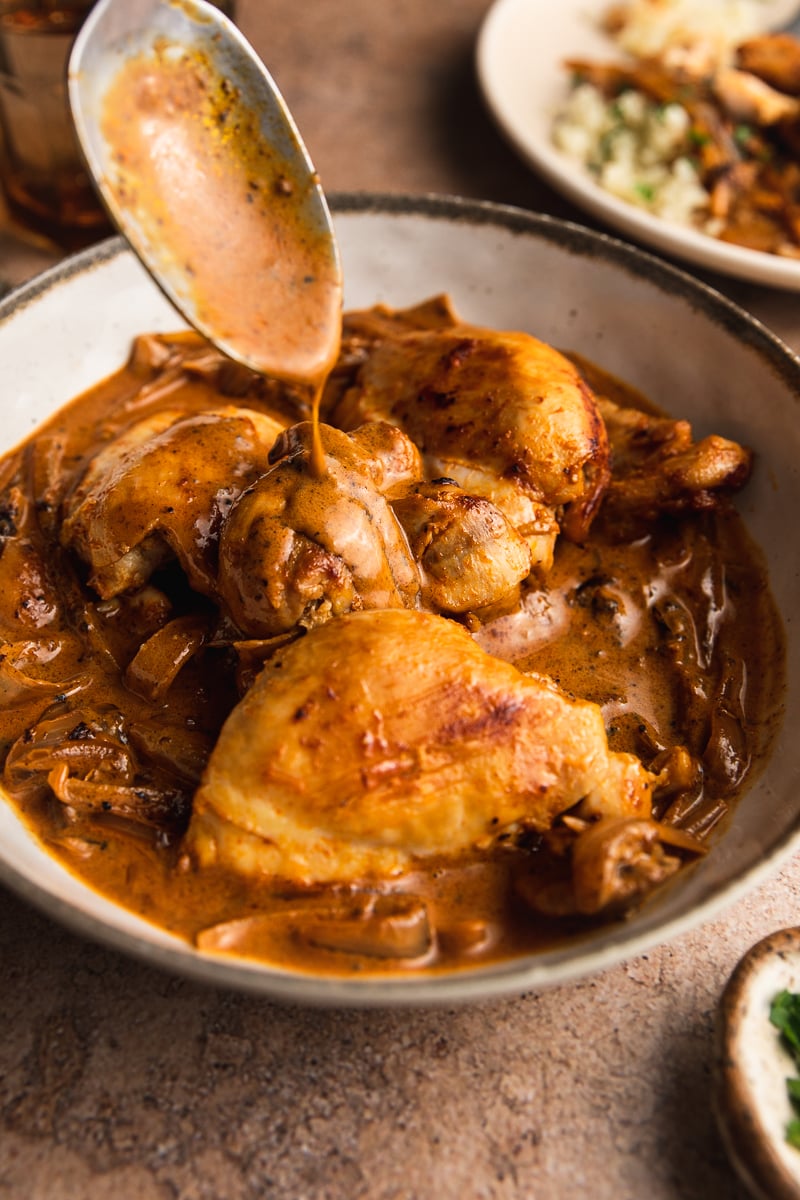 Creamy paprika chicken in a bowl with a spoon drizzling extra sauce on top.