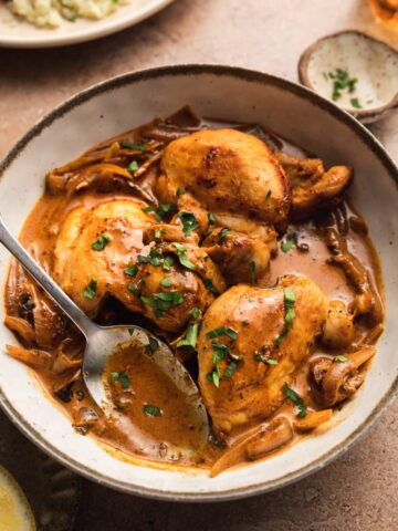 Creamy paprika chicken thighs in a bowl topped with parsley.