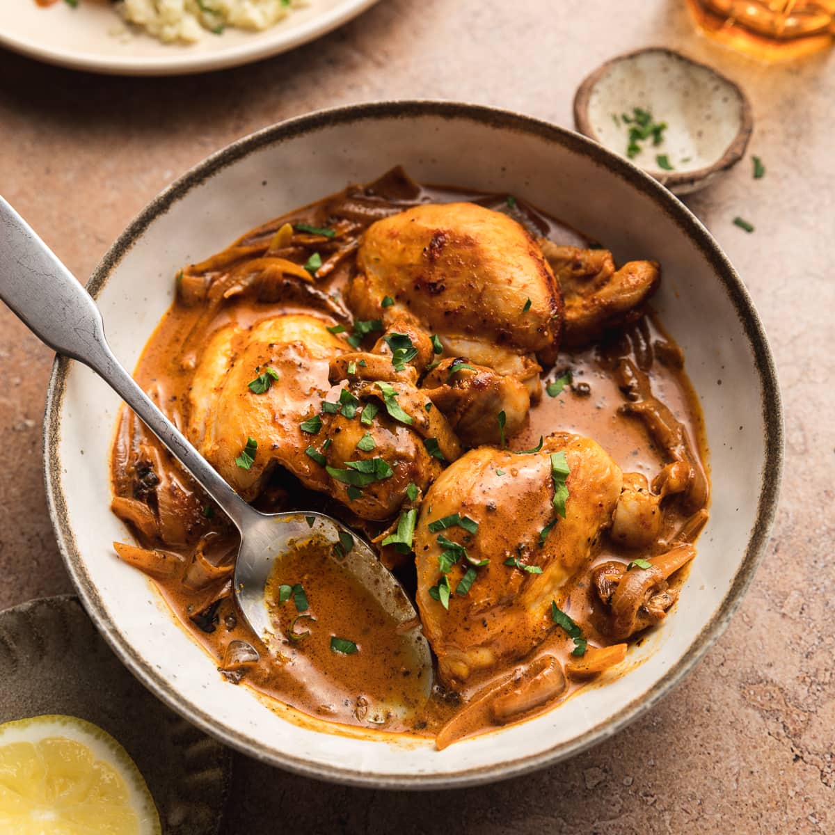 Creamy paprika chicken thighs in a bowl topped with parsley.