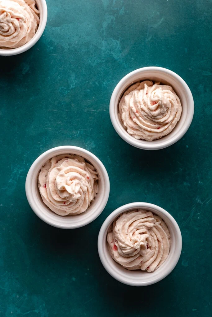Four white ramekins with keto strawberry mousse piped into servings.