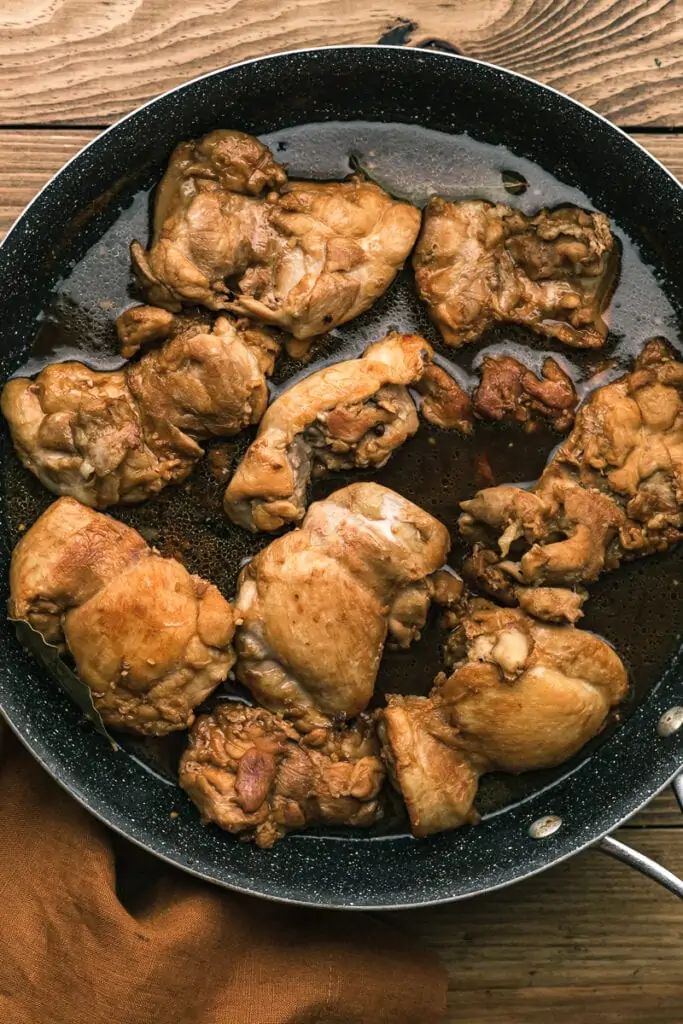 Chicken thighs cooking in adobo sauce in skillet.