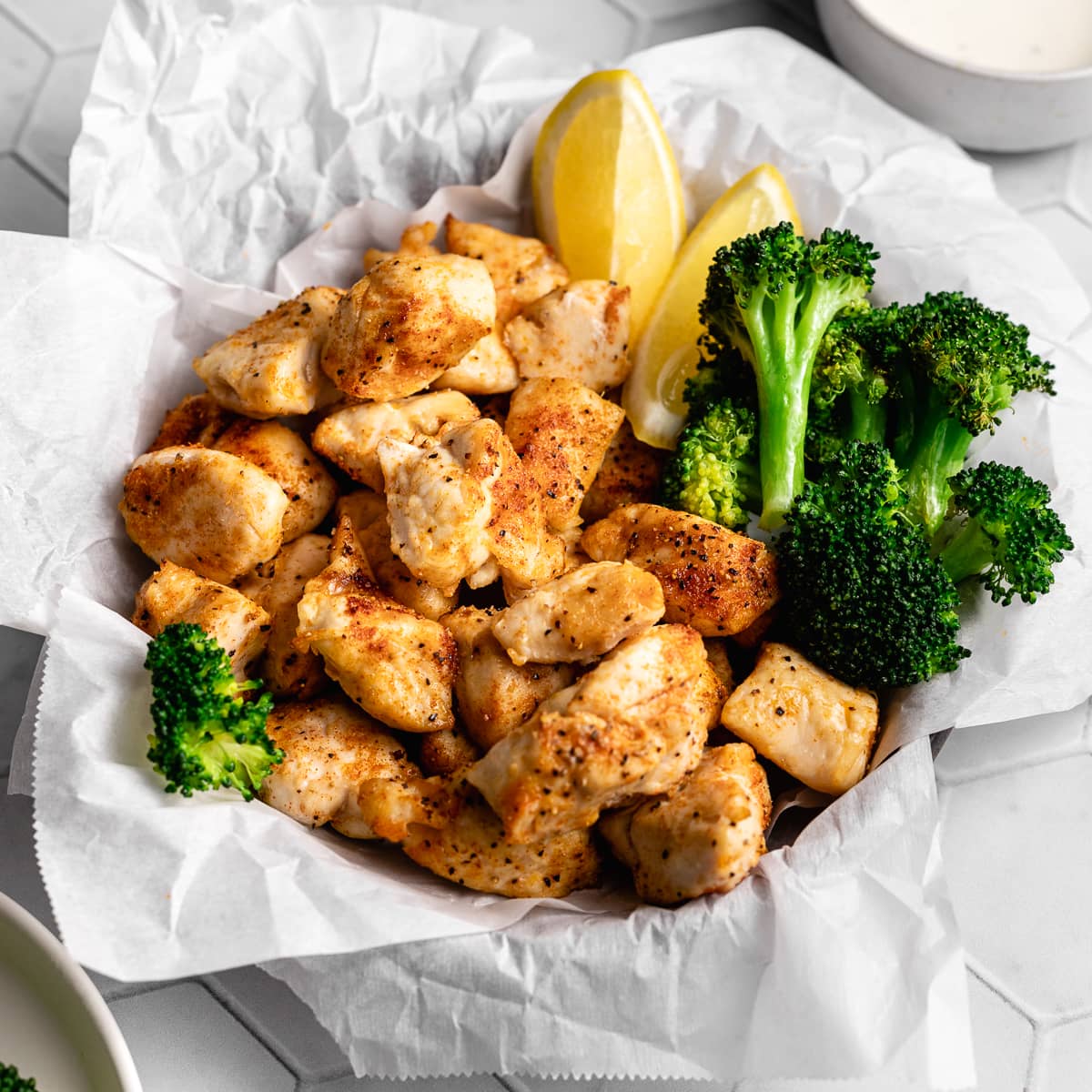 Air fryer chicken bites with broccoli and lemon wedges plated.