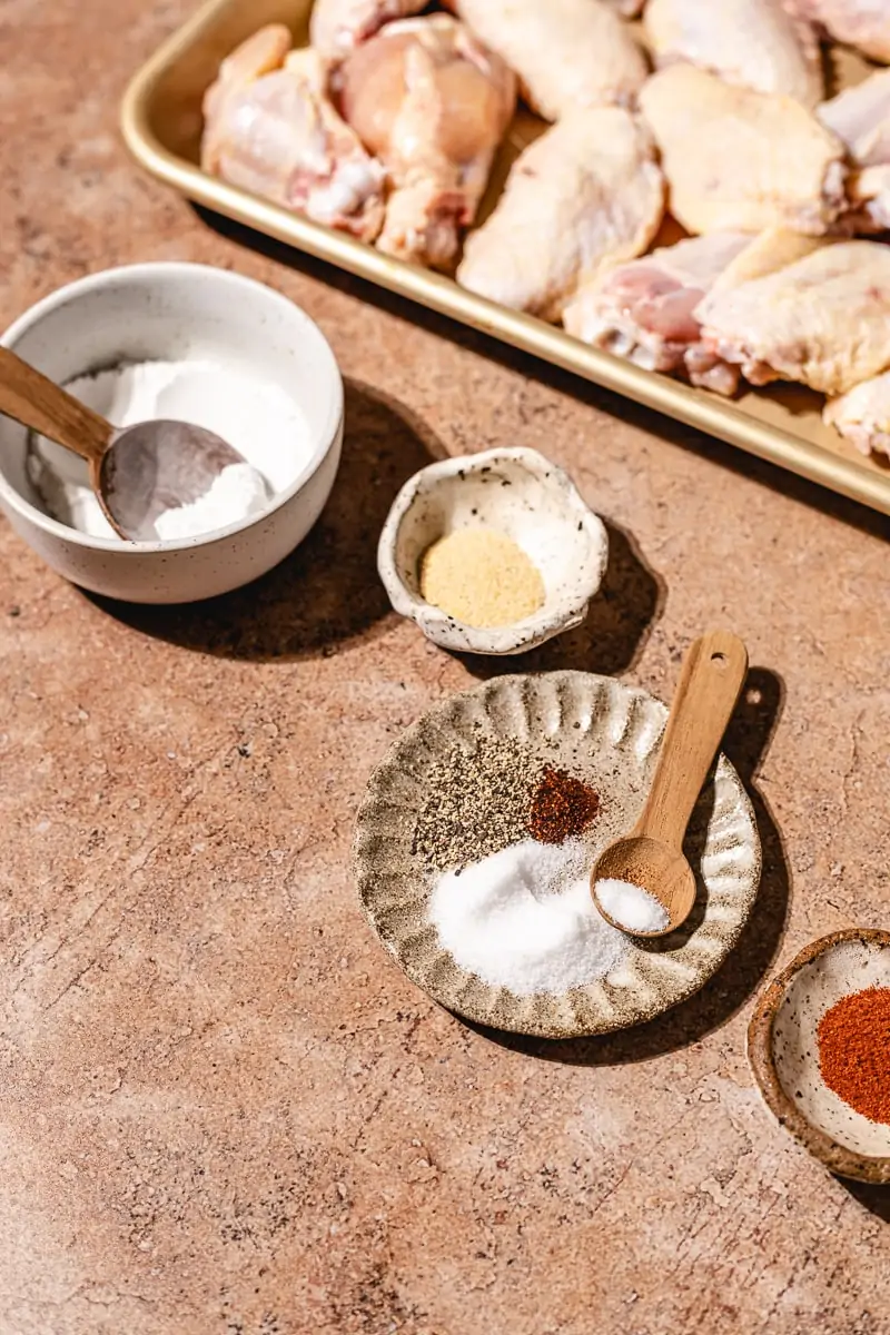 Spices and seasonings with raw chicken wings in background.