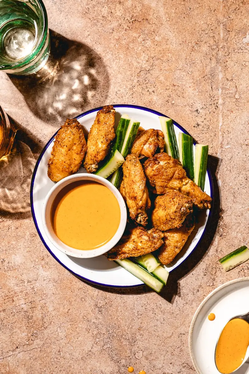Crispy air fryer chicken wings on a plate with cucumber wedges and two glasses.