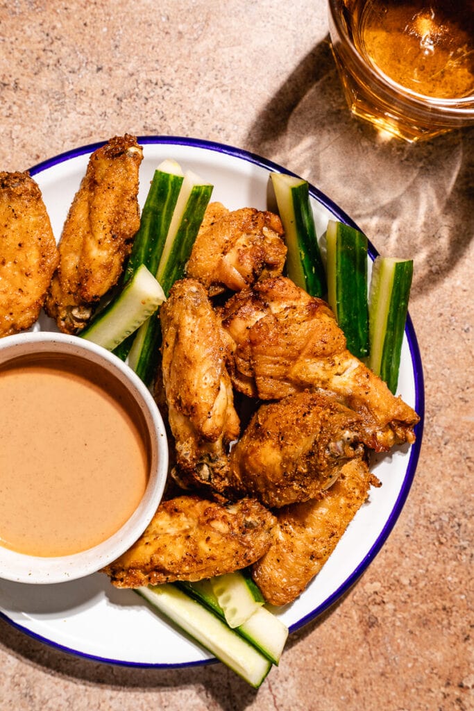 Overhead image of crispy air fryer chicken wings on a blue rimmed plate with cucumber sticks.