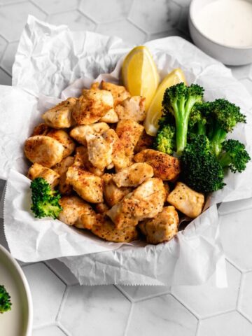 Air fryer chicken bites with broccoli and lemon wedges.